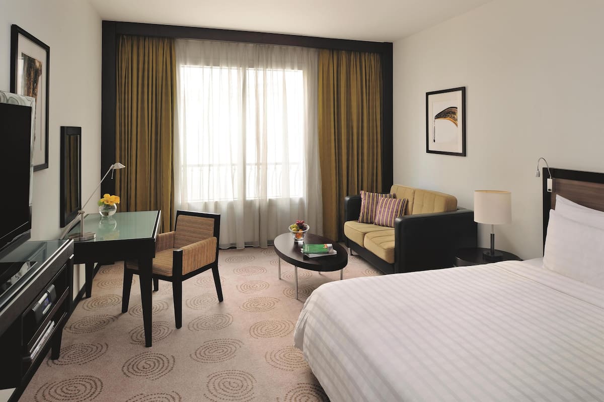 A hotel room with a bed, a desk, a chair, a sofa, a TV, and a window with curtains.