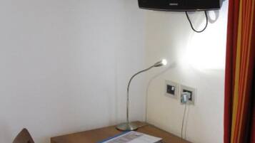 A small room with a wooden desk, a chair, a television mounted on the wall, and a lamp.