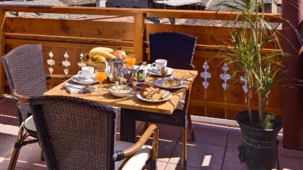 A wooden table set with breakfast items, overlooking a mountainous landscape. - Hotel Sassella (Grosio)