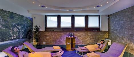 A spa area with two reclining chairs, a massage table, and a wall mural.