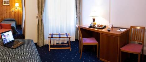 Habitación de hotel con cama, escritorio, silla, televisor y ventana con cortinas.