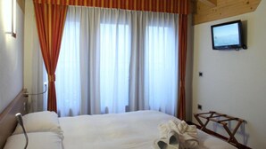 A hotel room with a bed, curtains, a television, and a wooden ceiling. - Hotel Sassella (Grosio)