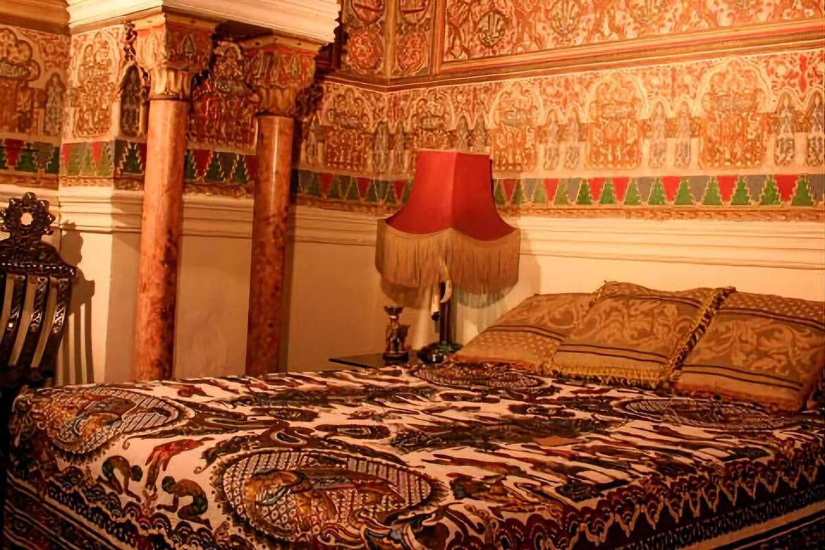A room with ornate, patterned walls and a large bed with a red lamp.