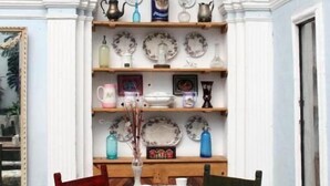 Comedor con mesa y sillas de madera, rodeado de estanterías con platos y cerámica.