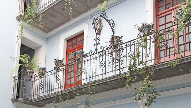 Un café al aire libre con mesas y sillas de madera, una puerta roja y estantes decorativos.