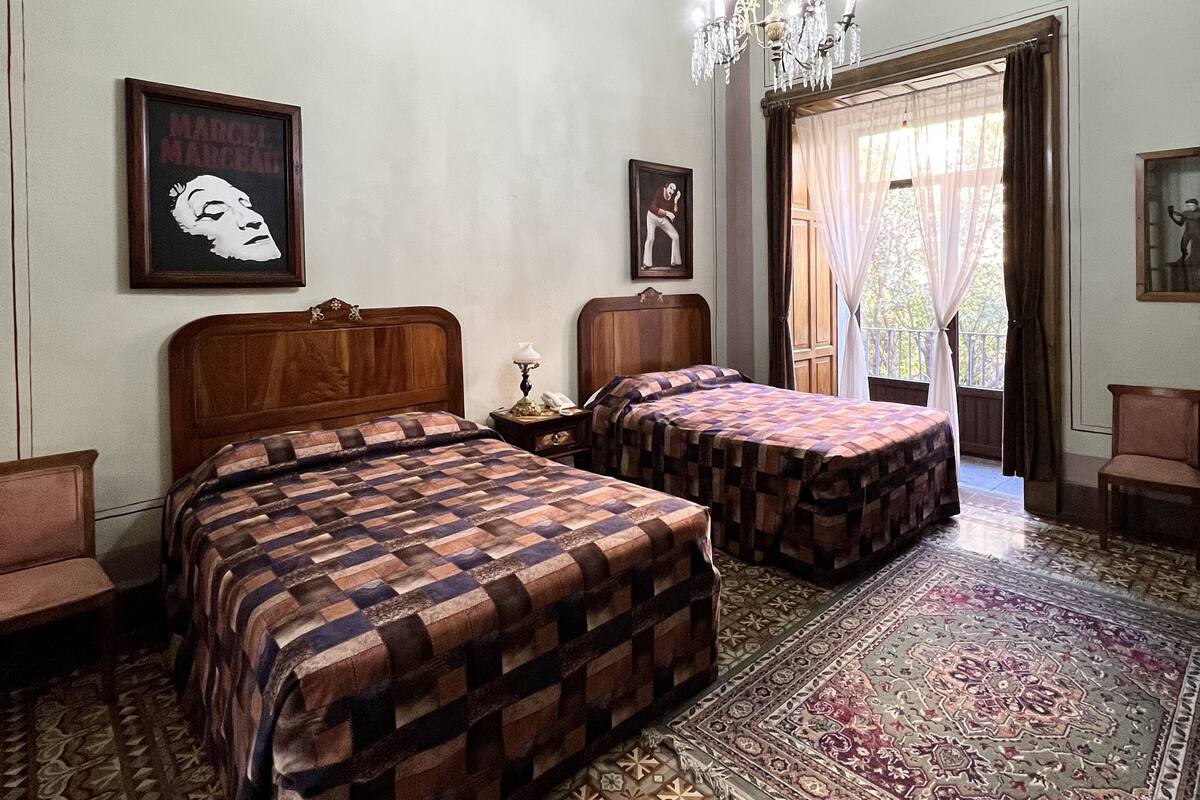 A room with two beds, a chandelier, and a patterned rug.