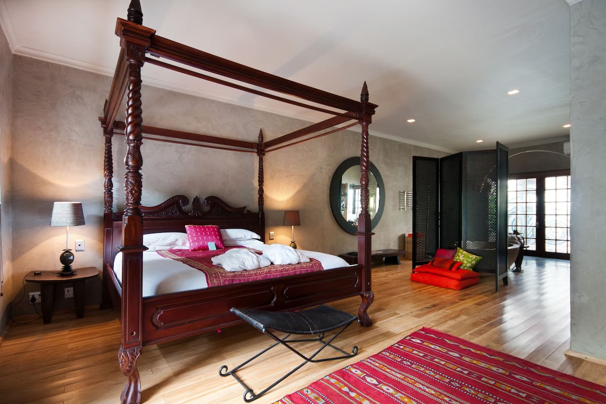 Een hemelbed met voeteneind, een nachtkastje met lamp, een rode bank en een grote spiegel aan de muur.