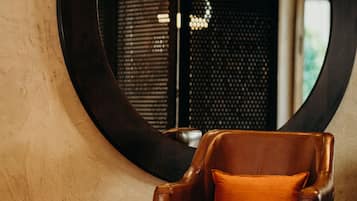 A leather armchair with an orange cushion in front of a round mirror on a textured wall.