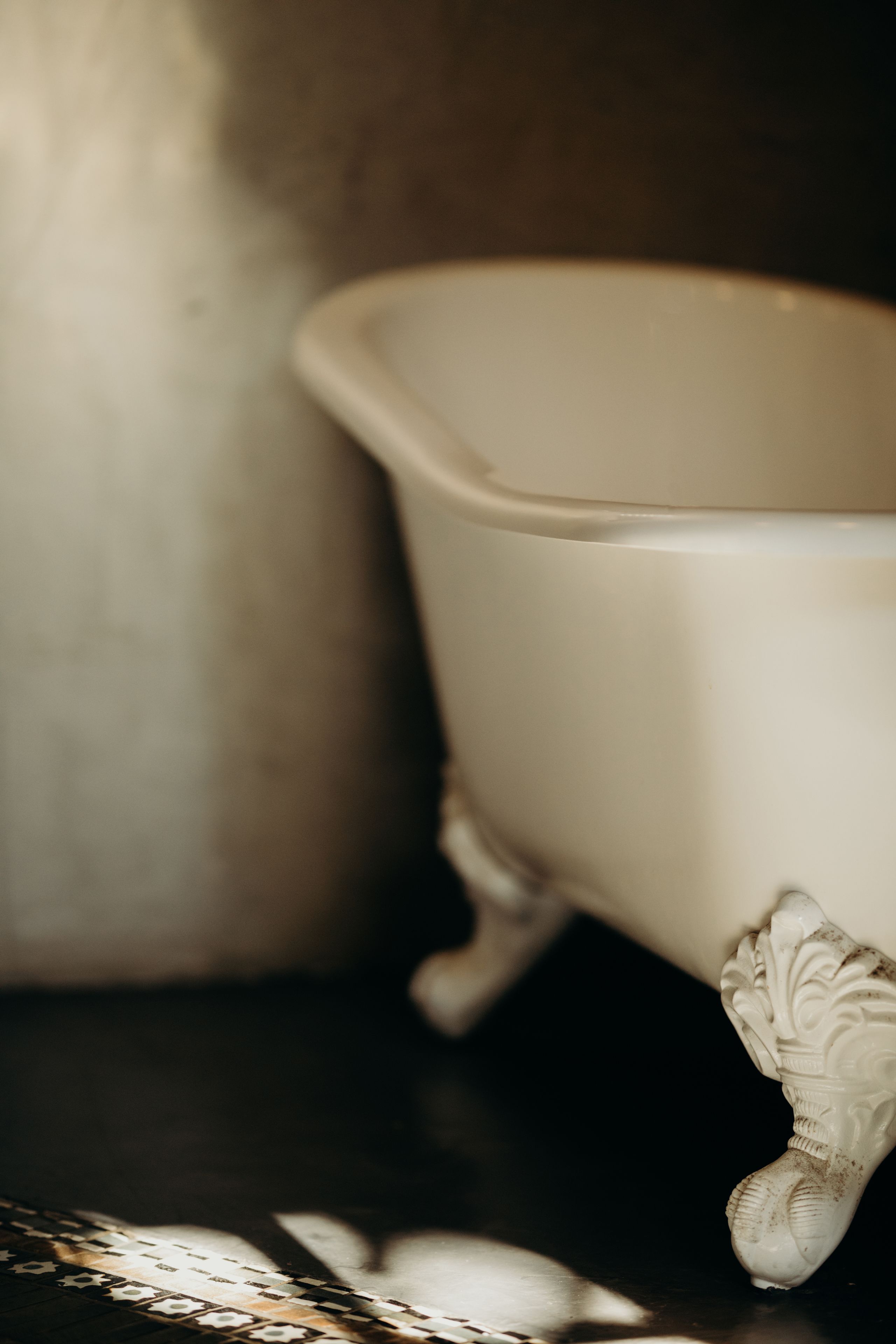 Una bañera con patas ornamentadas, piso de baldosas y pared lisa.