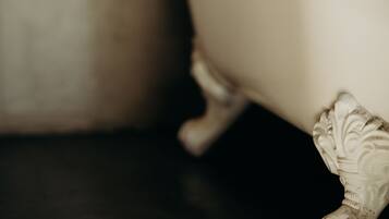 Una bañera con patas ornamentadas, piso de baldosas y pared lisa.