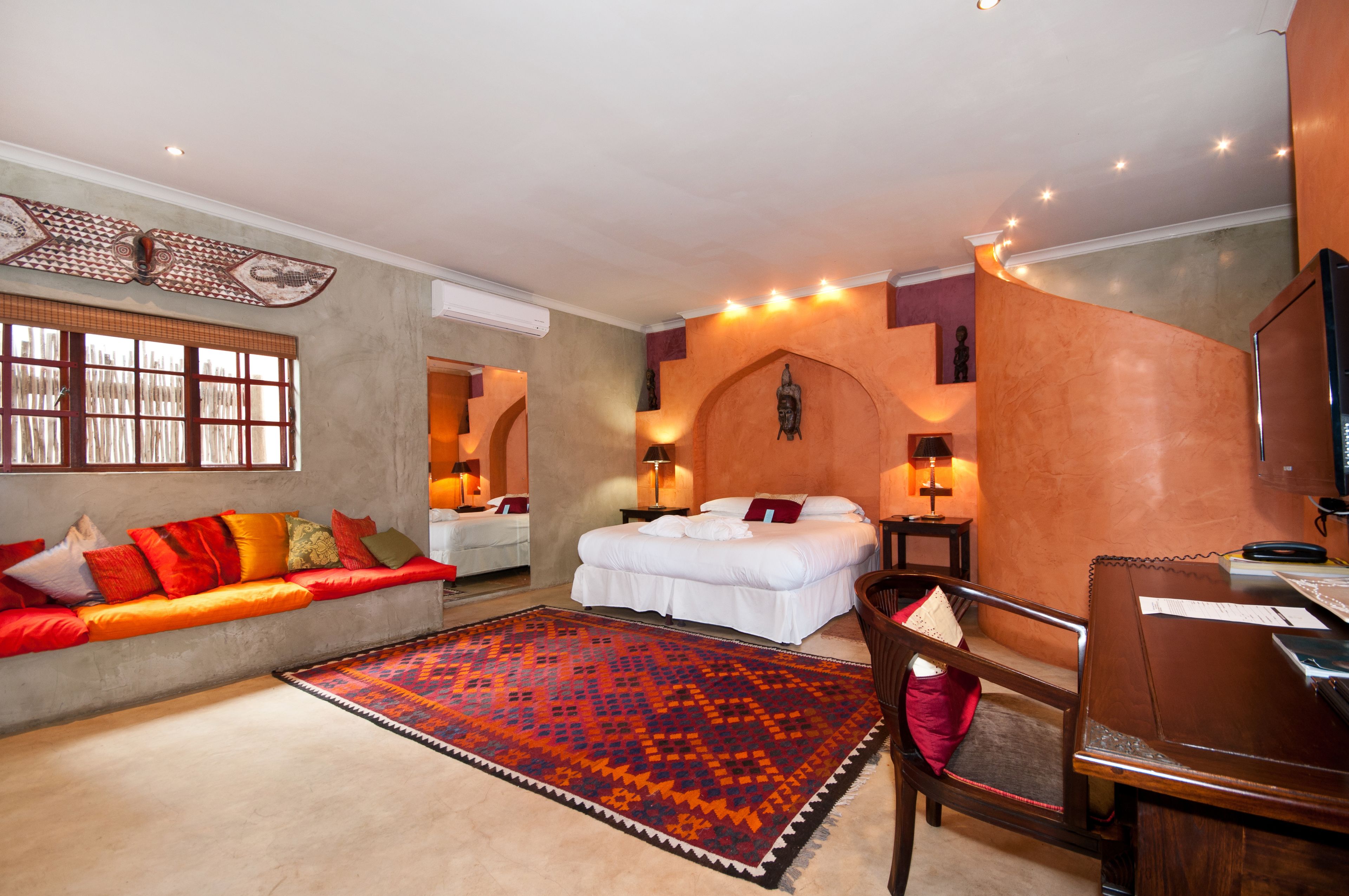 Una camera d'albergo con un letto, un divano con cuscini colorati, una scrivania in legno e un tappeto decorato.