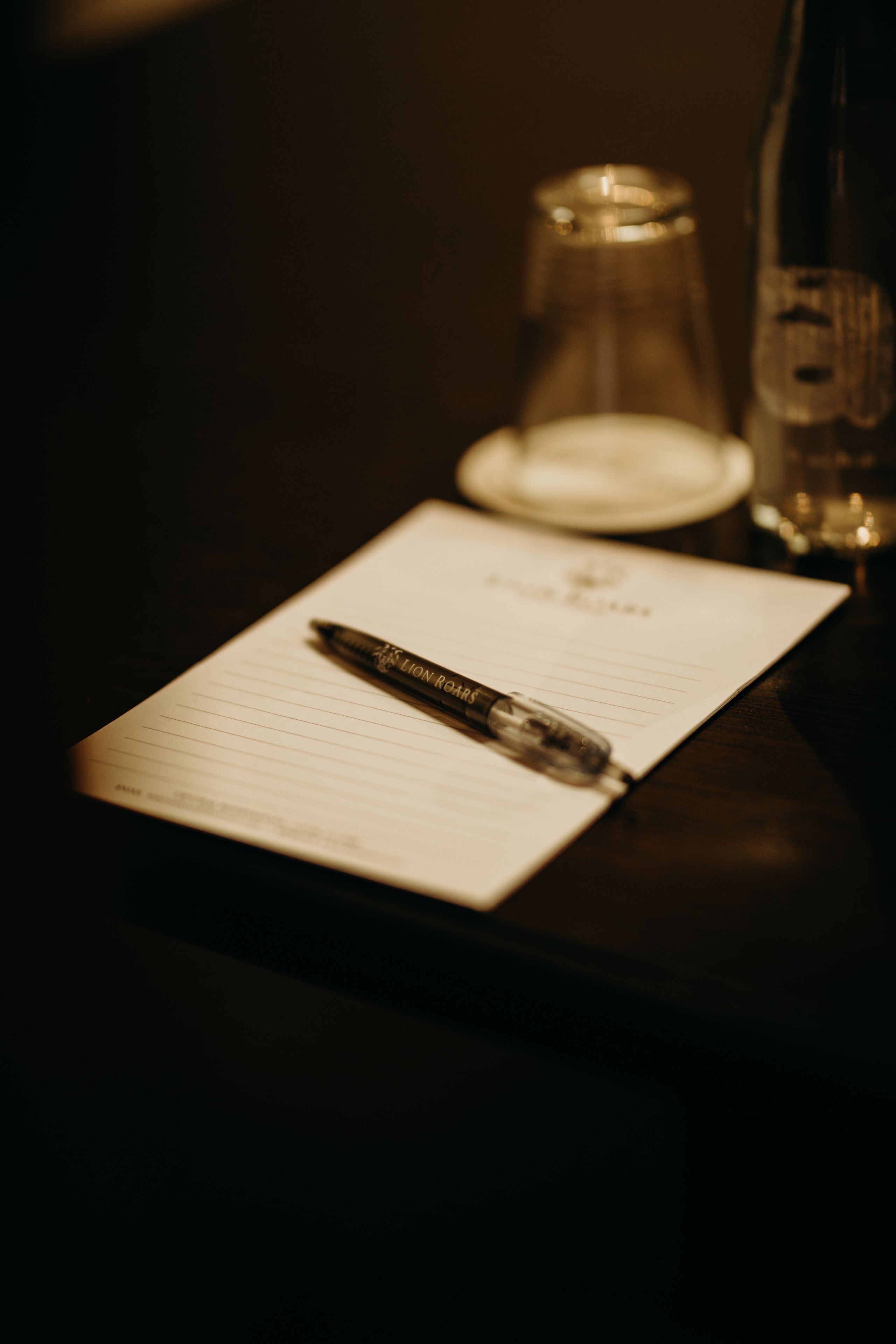 Un carnet avec un stylo posé sur une surface sombre, une bouteille en verre et un verre.