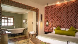 Habitación de hotel con bañera, cama con almohadillas verdes, banca de madera con comida y bebida, y pared con diseño.