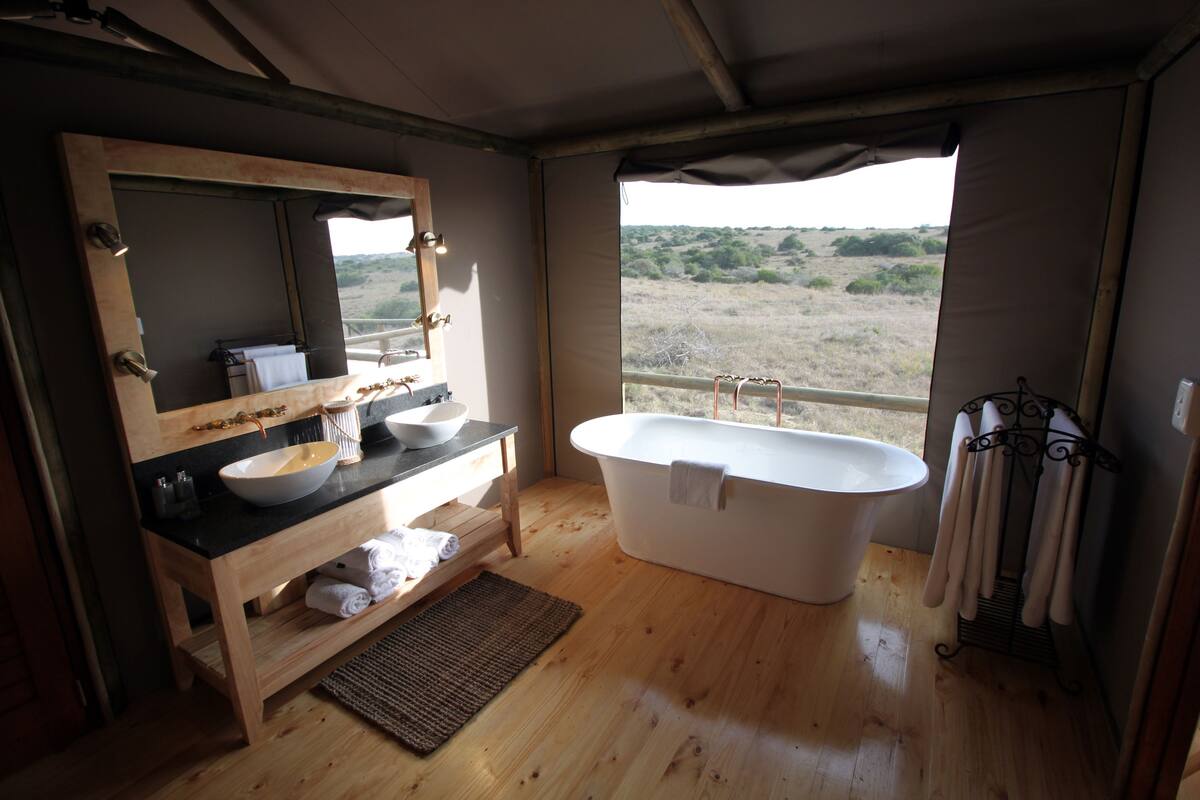 Un baño moderno con una bañera grande, un tocador de madera con lavamanos y espejo, y vistas al exterior.