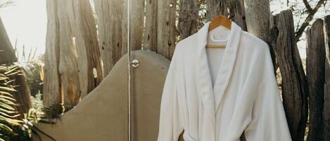 A white bathrobe hanging on a wooden hanger, a showerhead, and a wooden fence with trees in the background.