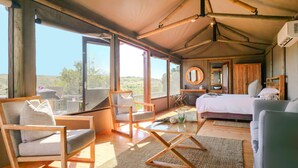 Une pièce spacieuse avec un grand lit, un bureau en bois, une chaise et un canapé. De grandes fenêtres offrent une vue sur l’extérieur.