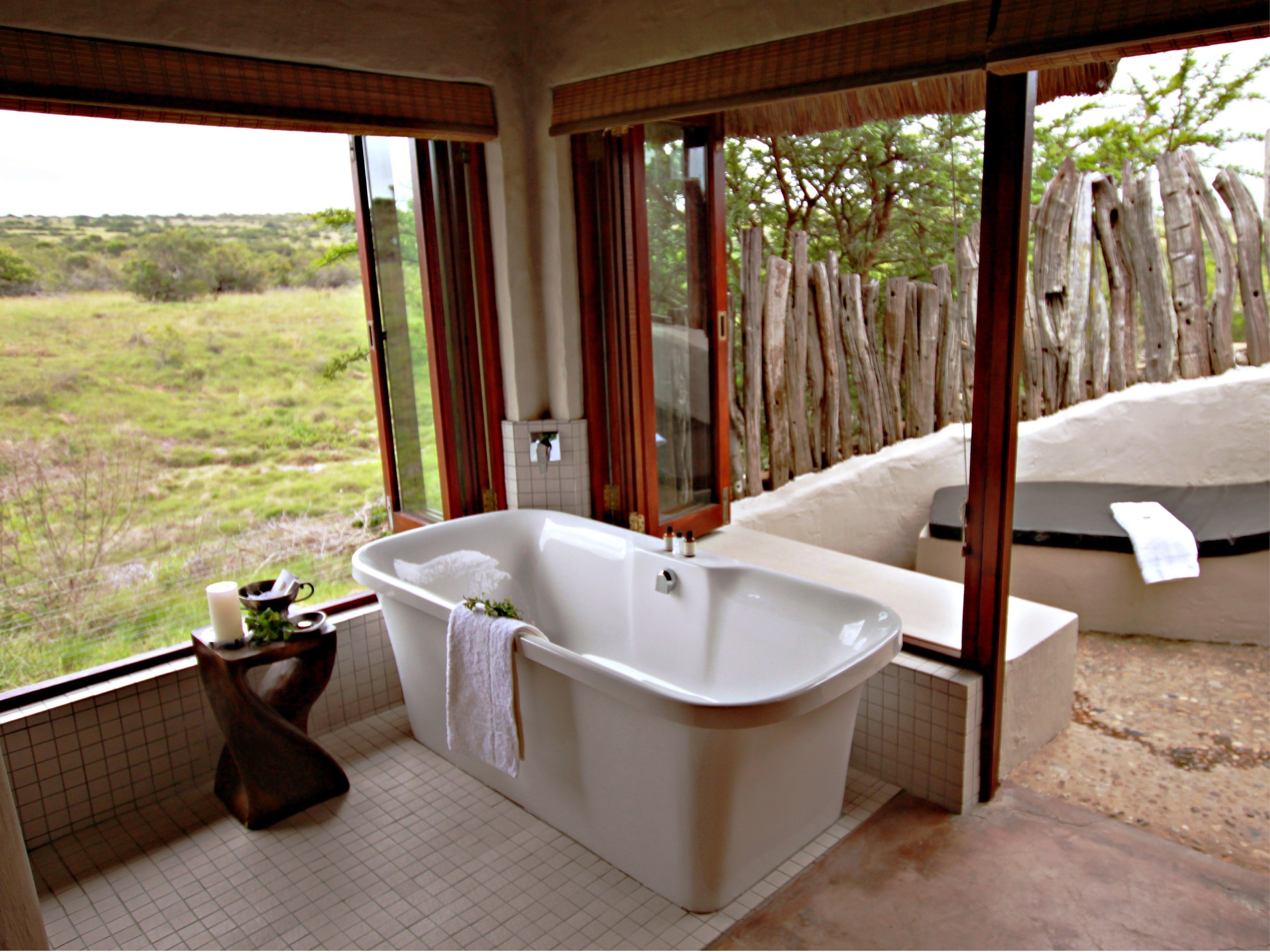 Un baño con una bañera grande, un espejo y una ventana con vistas a un paisaje natural.