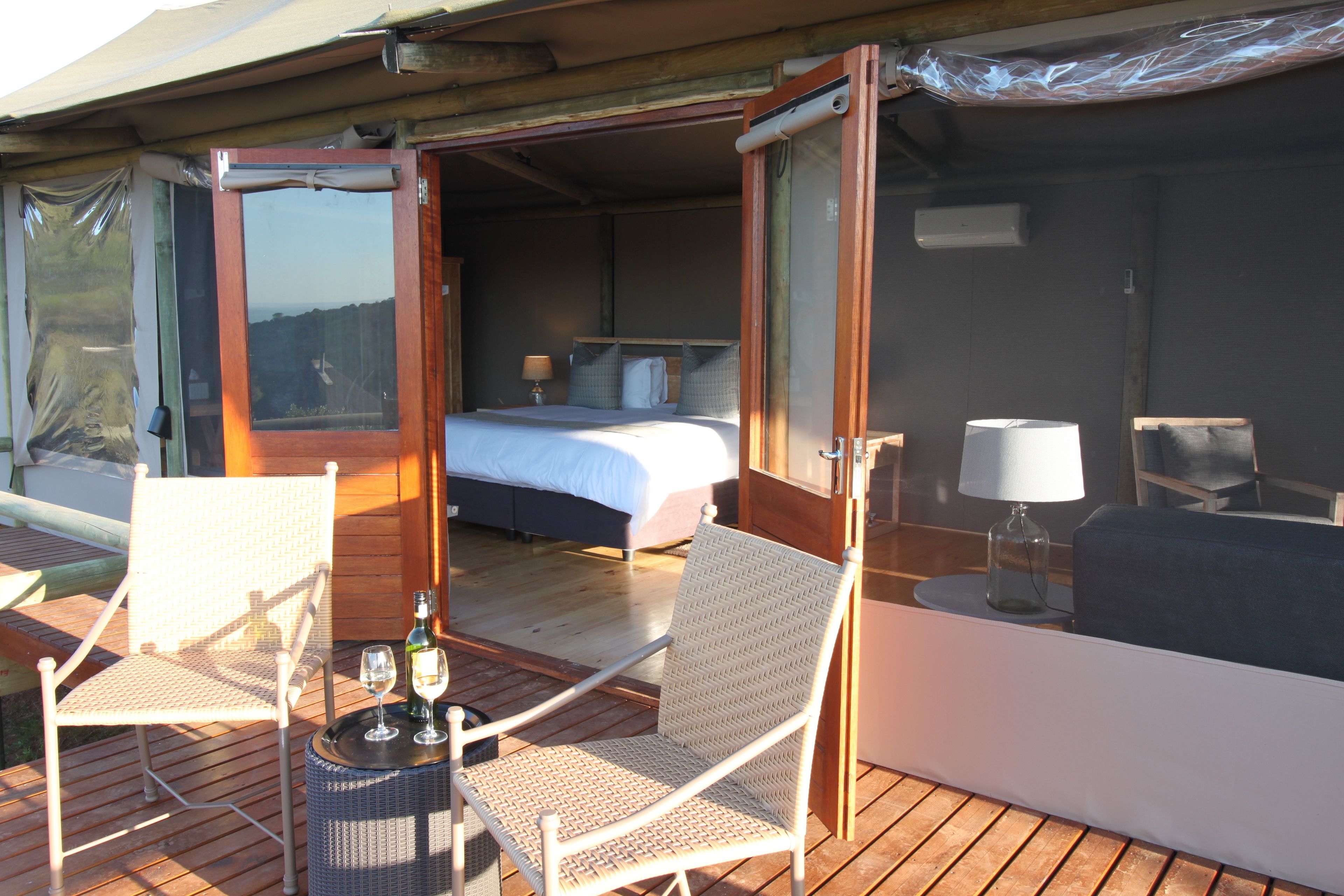 Ein helles Schlafzimmer mit einem Bett, zwei Stühlen, einem Tisch mit Flasche und Glas und Blick ins Freie.