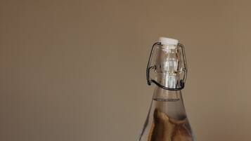 Una botella de vidrio transparente con un cierre metálico, sobre una superficie de madera con varias copas de vidrio transparentes al fondo.