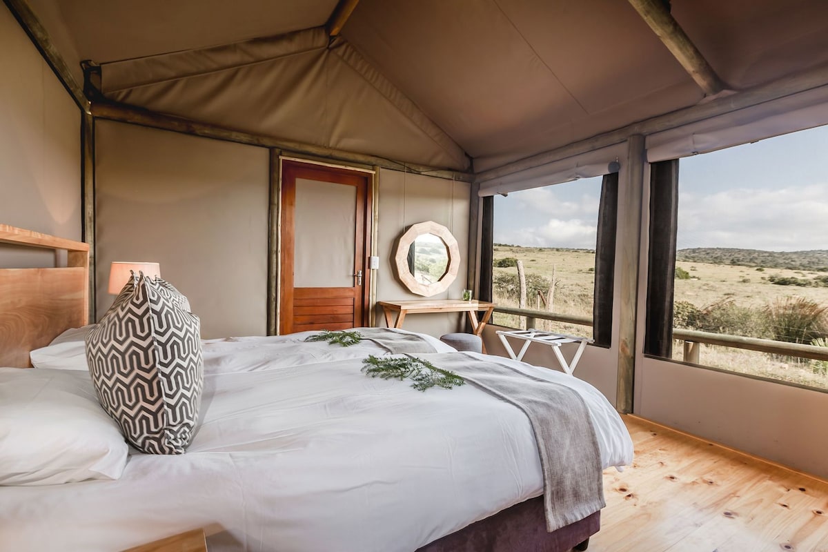 Une chambre à coucher avec un lit, une tête de lit en bois, une table de chevet, un miroir et une vue sur l’extérieur.