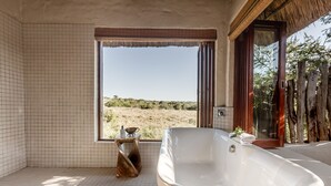 Une salle de bain avec une grande baignoire, une fenêtre donnant sur le désert et une petite table avec un bol et une bouteille.