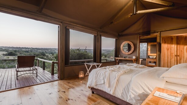 Une chambre avec un grand lit, une table de chevet en bois, une chaise, une petite table et une fenêtre donnant sur le paysage.