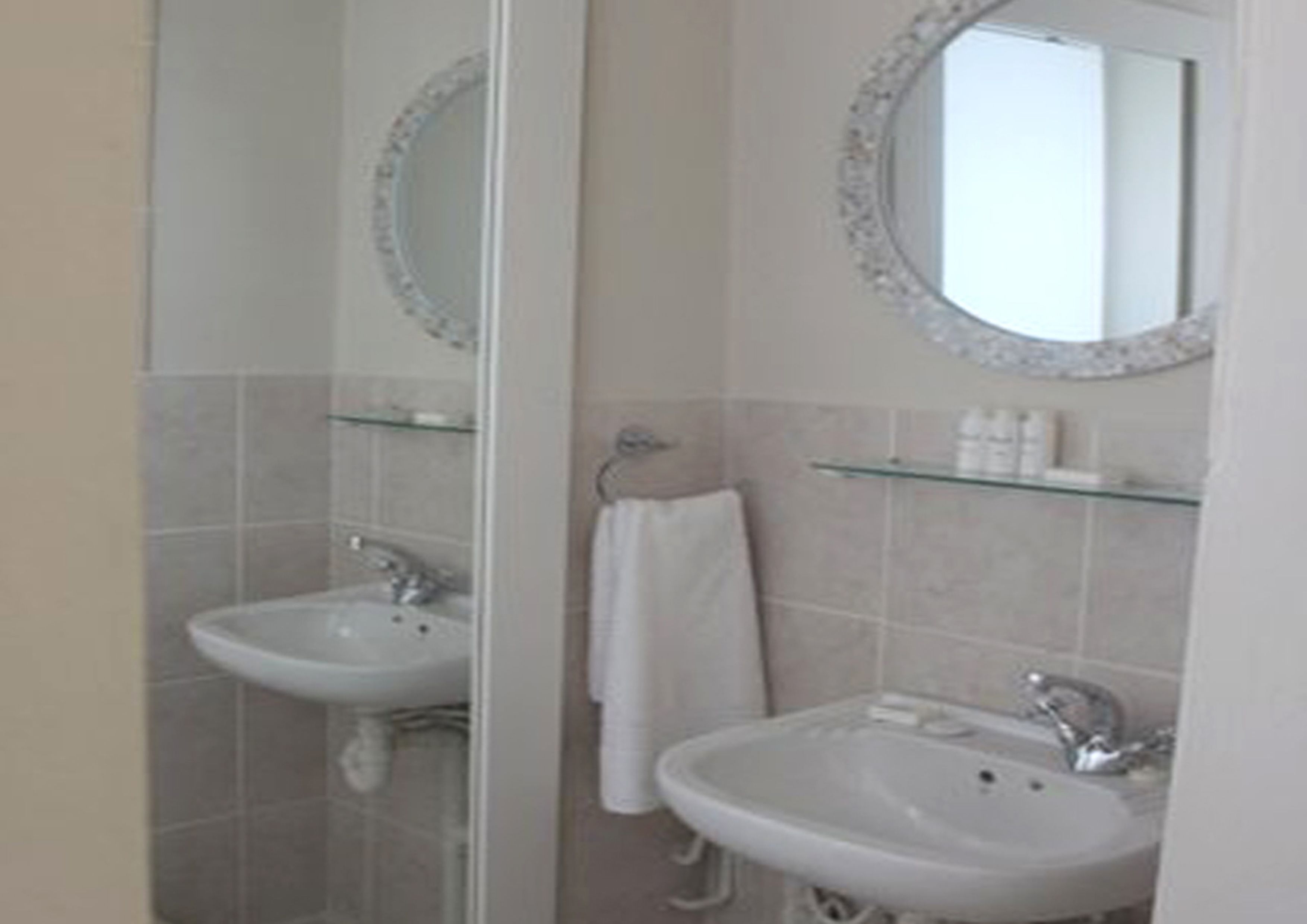 A bathroom with two sinks, a mirror, and a glass shelf with toiletries.