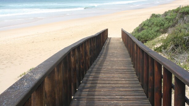 Une promenade en bois qui mène à une plage de sable et offre une vue sur l’océan.
