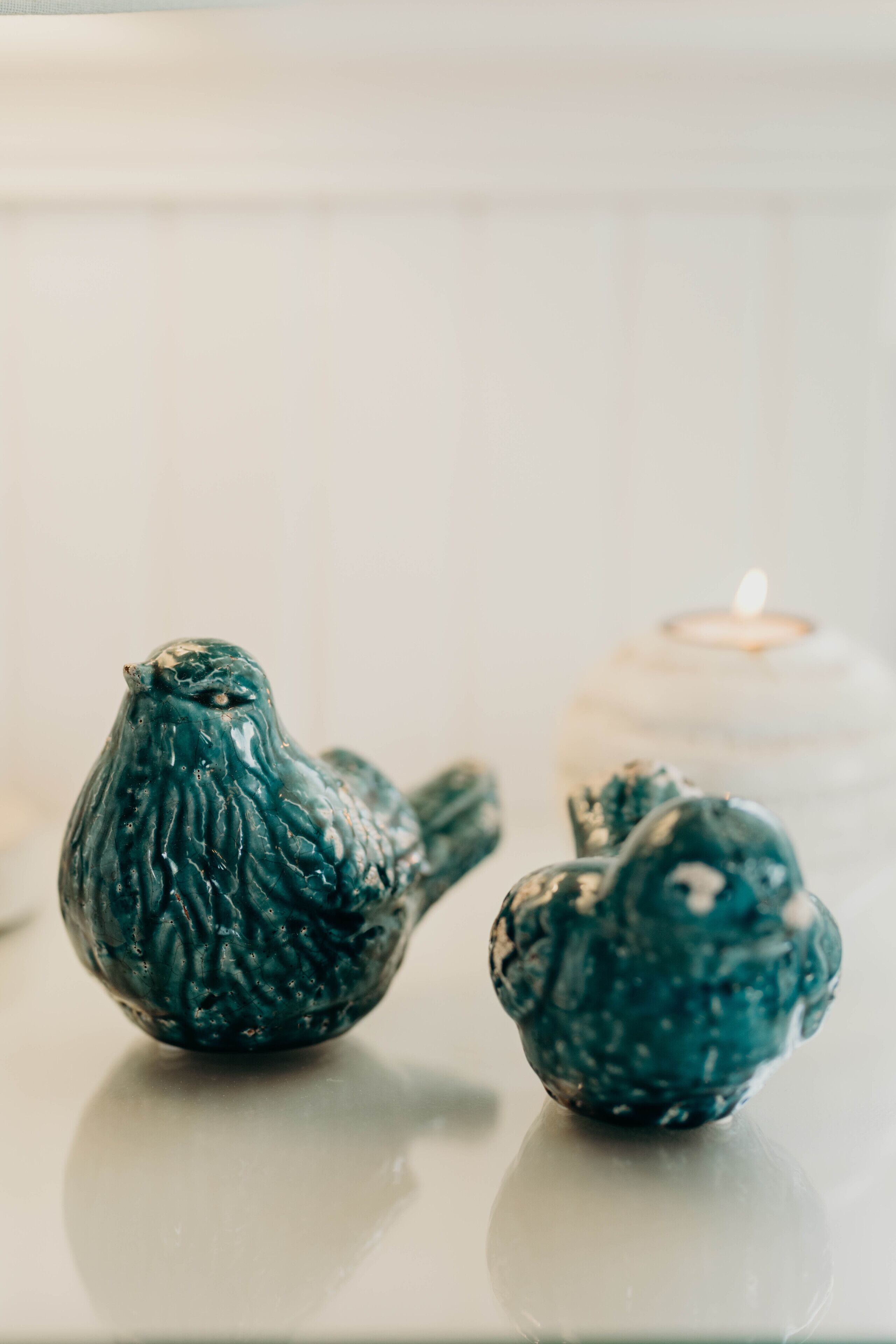 Two bird-shaped candle holders on a reflective surface with a lit candle in the background.