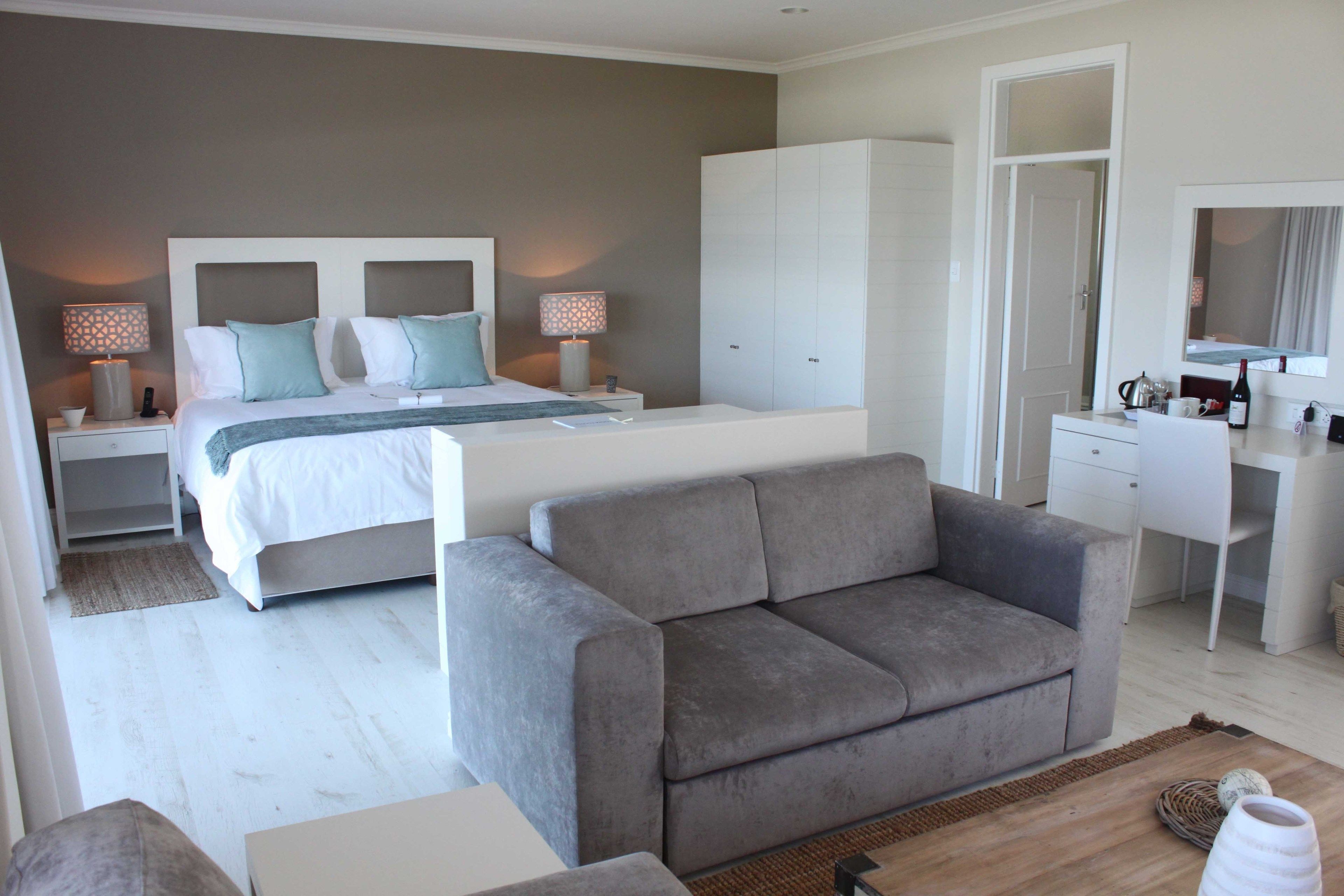 A modern bedroom with a large bed, a grey sofa, a wardrobe, and a desk with a mirror.