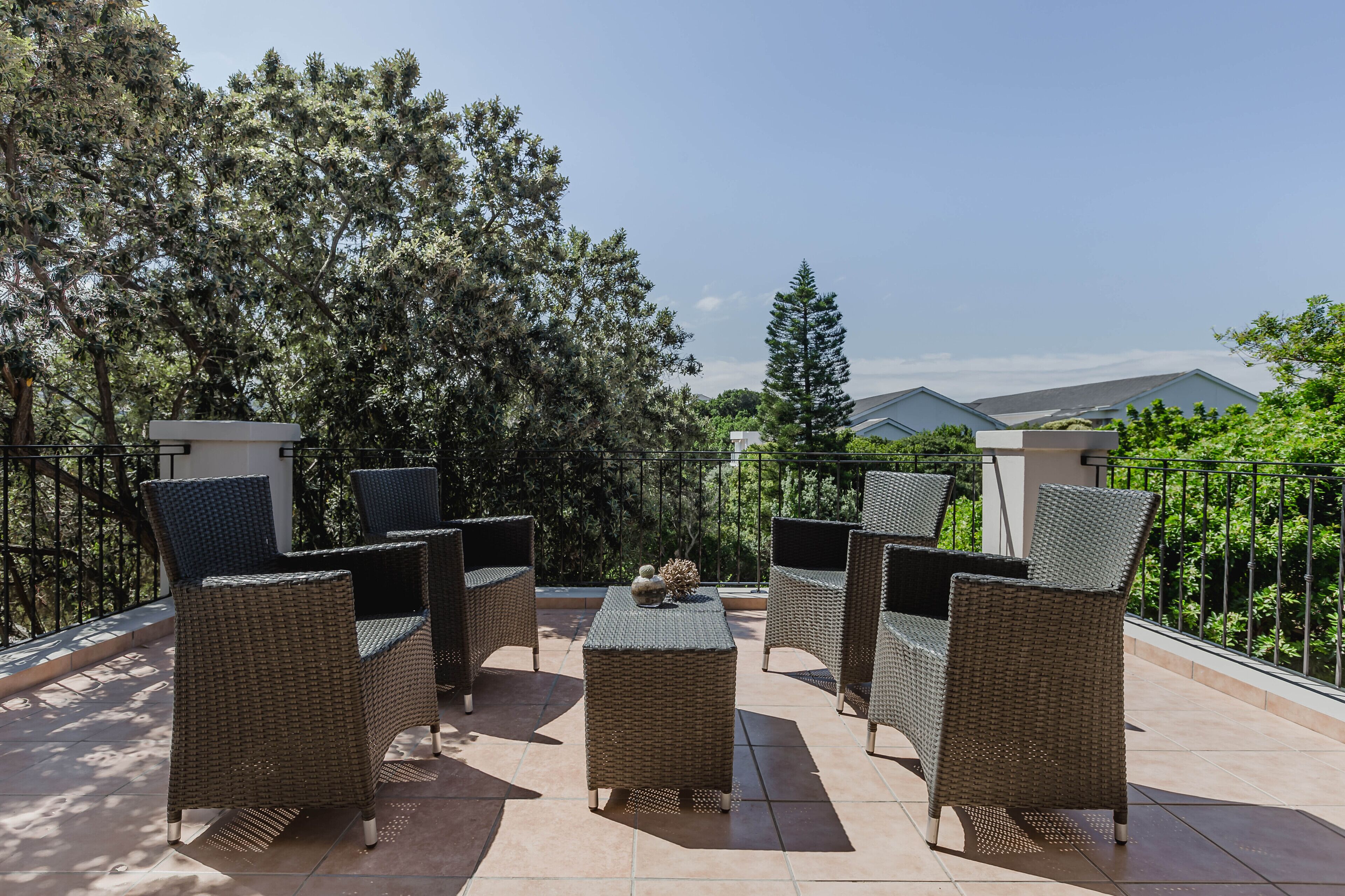 Una terraza con mobiliario de mimbre, una mesita y vistas a árboles y edificios.