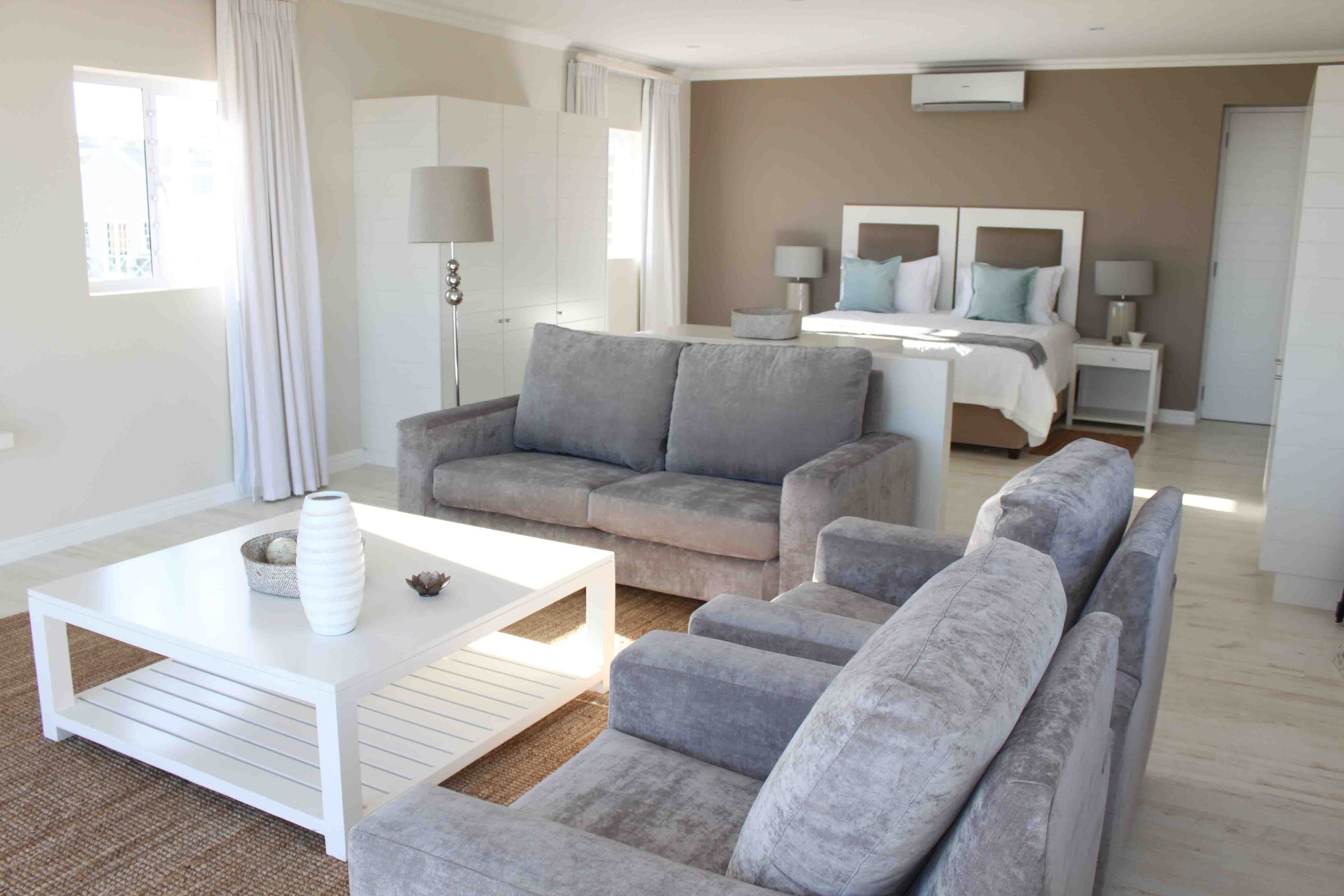 A modern hotel room with a grey sofa set, a white coffee table, and a bed with a white headboard.