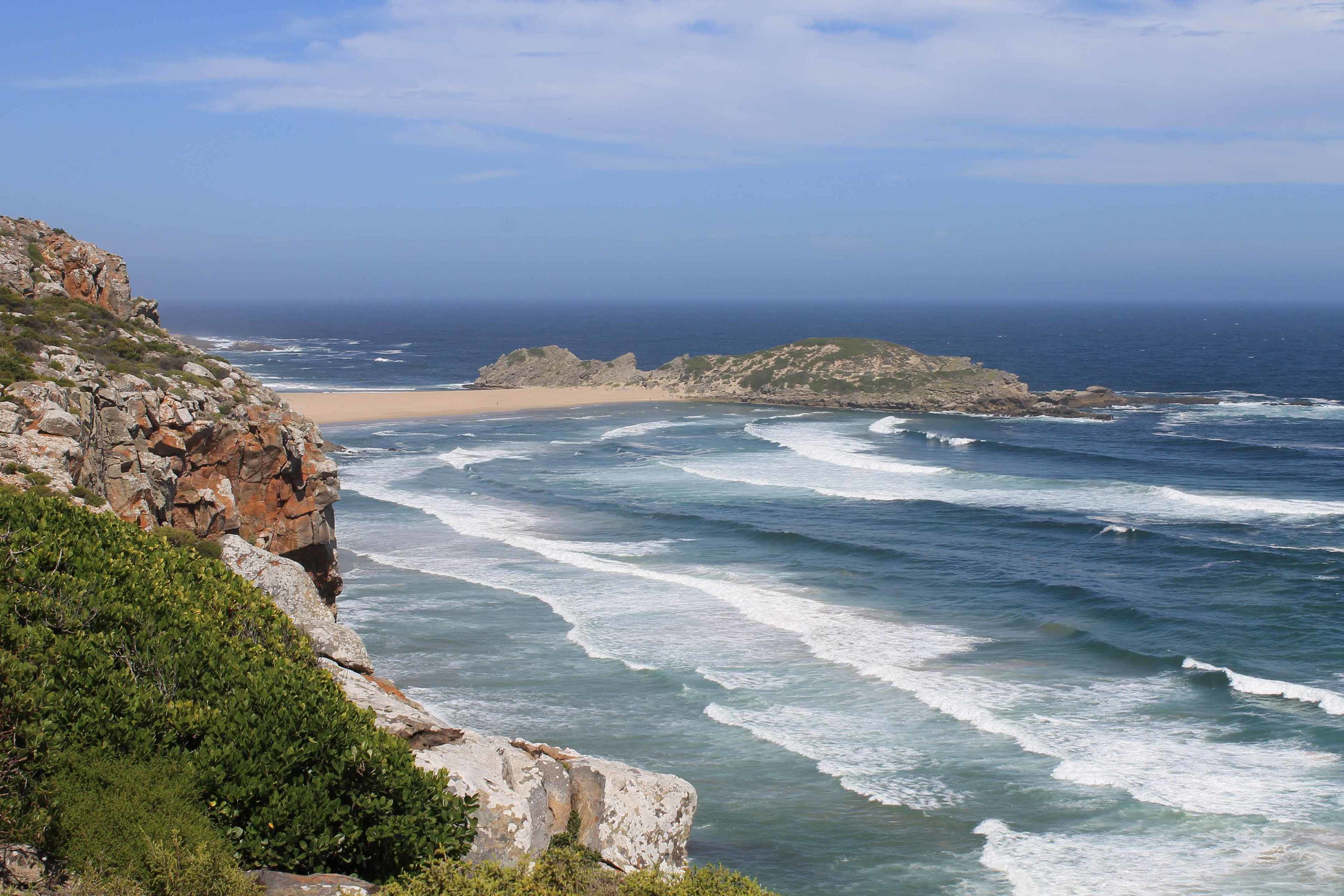 Un paysage côtier caractérisé par des falaises rocheuses, une plage de sable et des vagues qui déferlent sur le rivage.