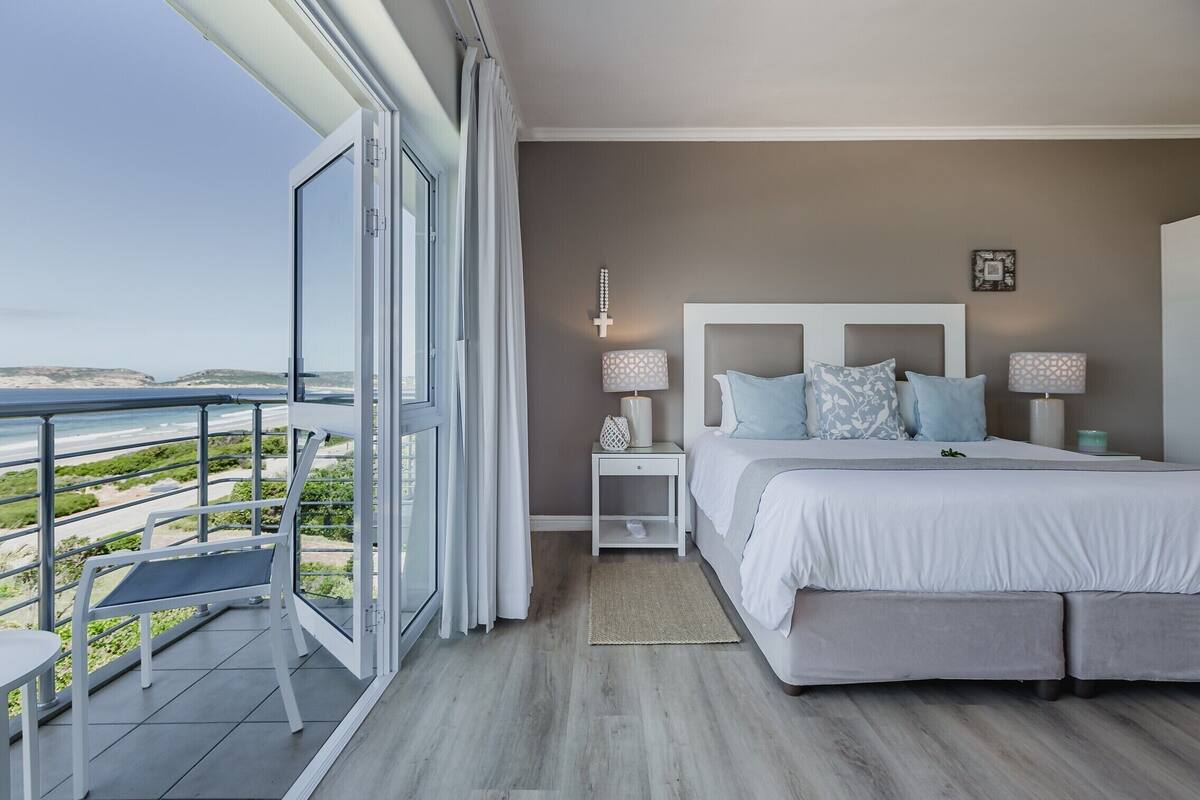 Une chambre avec un grand lit, une table de chevet, une lampe et une vue sur la plage.