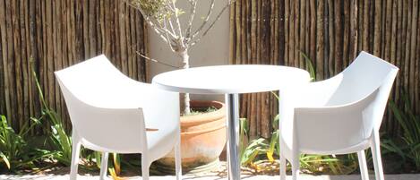 A round table with two white chairs in a garden area with a bamboo fence and potted plants.