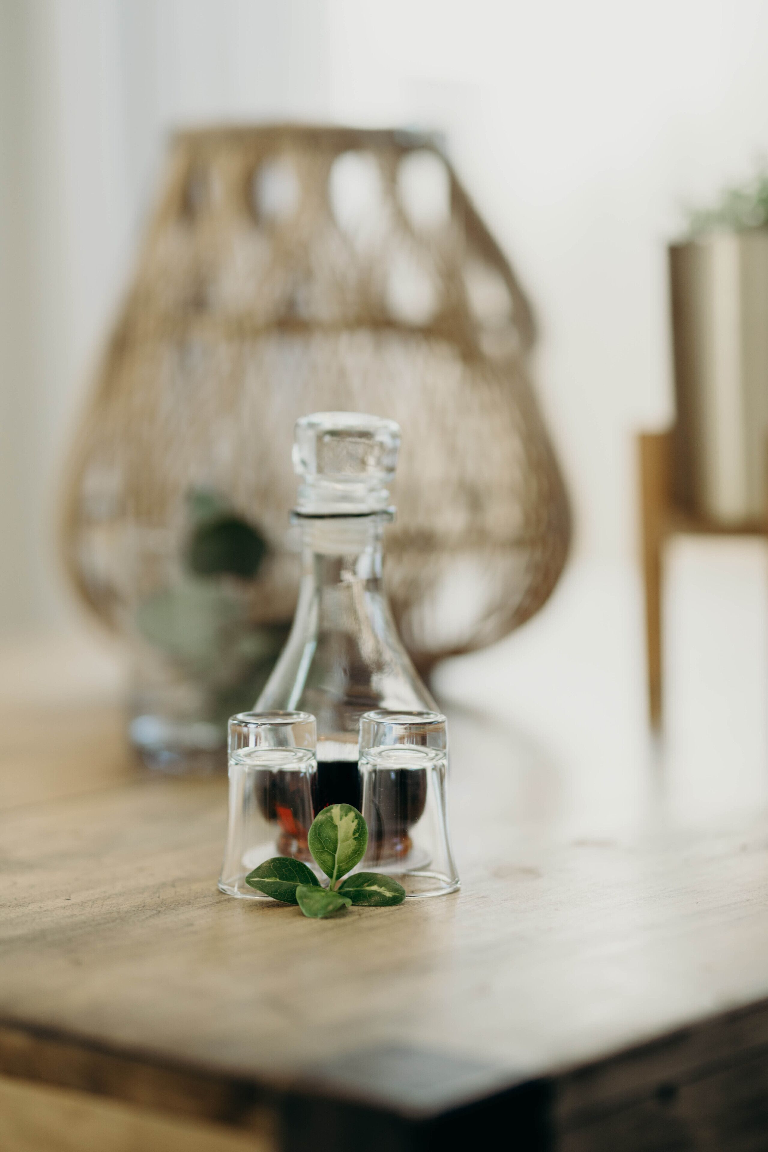 A clear glass bottle with a cork stopper and a small glass container with a plant on a wooden surface.
