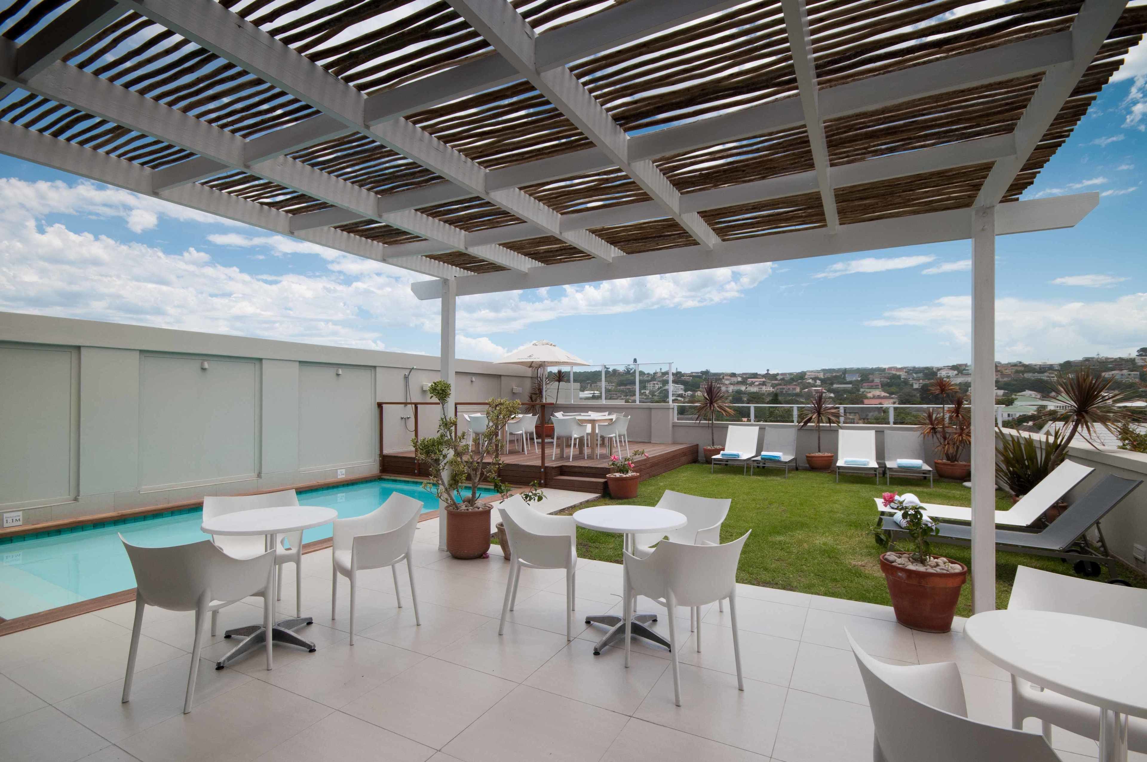 A rooftop patio with a pool, white chairs, and a view of the city.