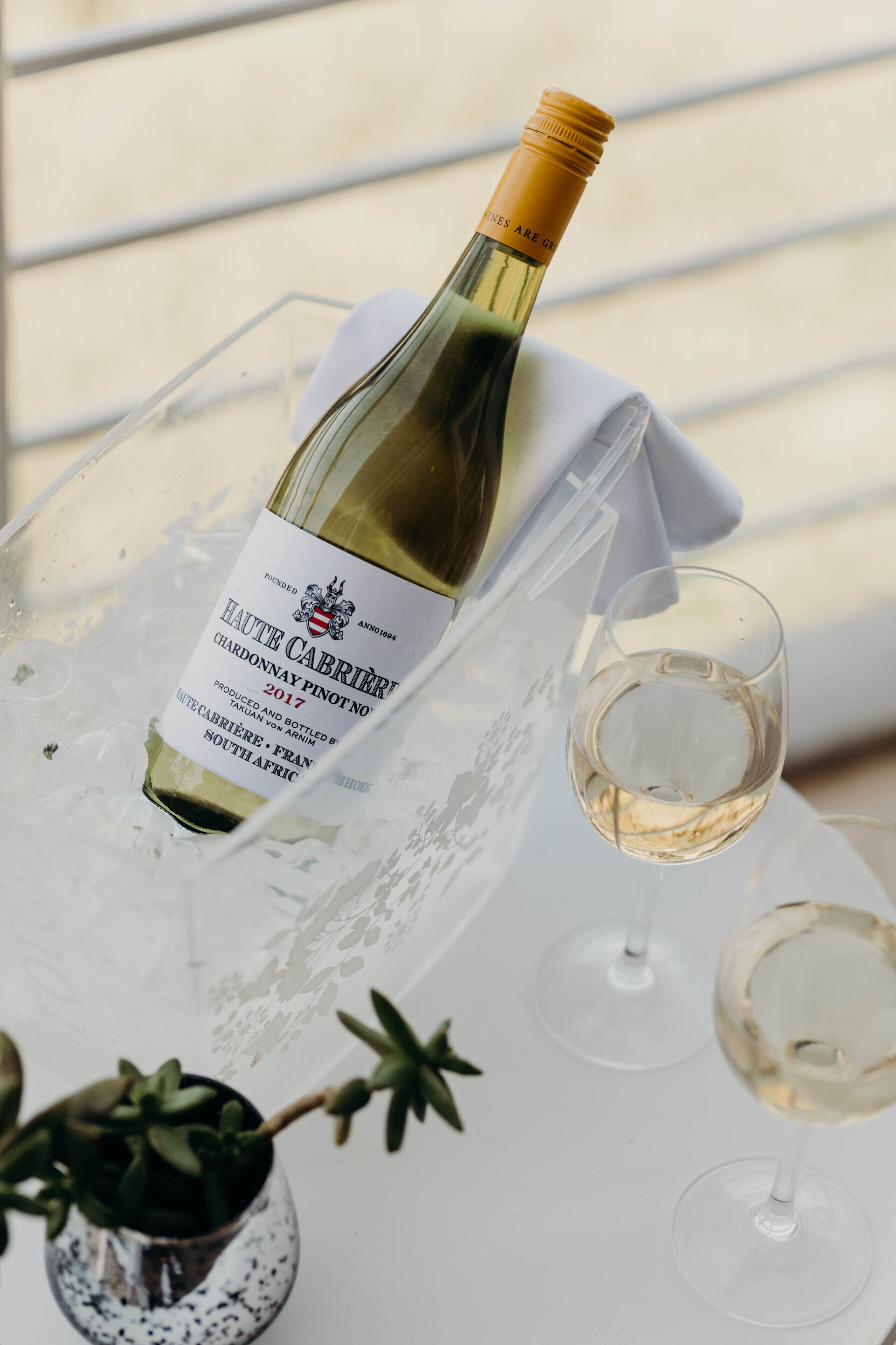 Una botella de Haut Cahrière 2017 Chardonnay Pinot Noir sobre una bandeja con una copa de vino.