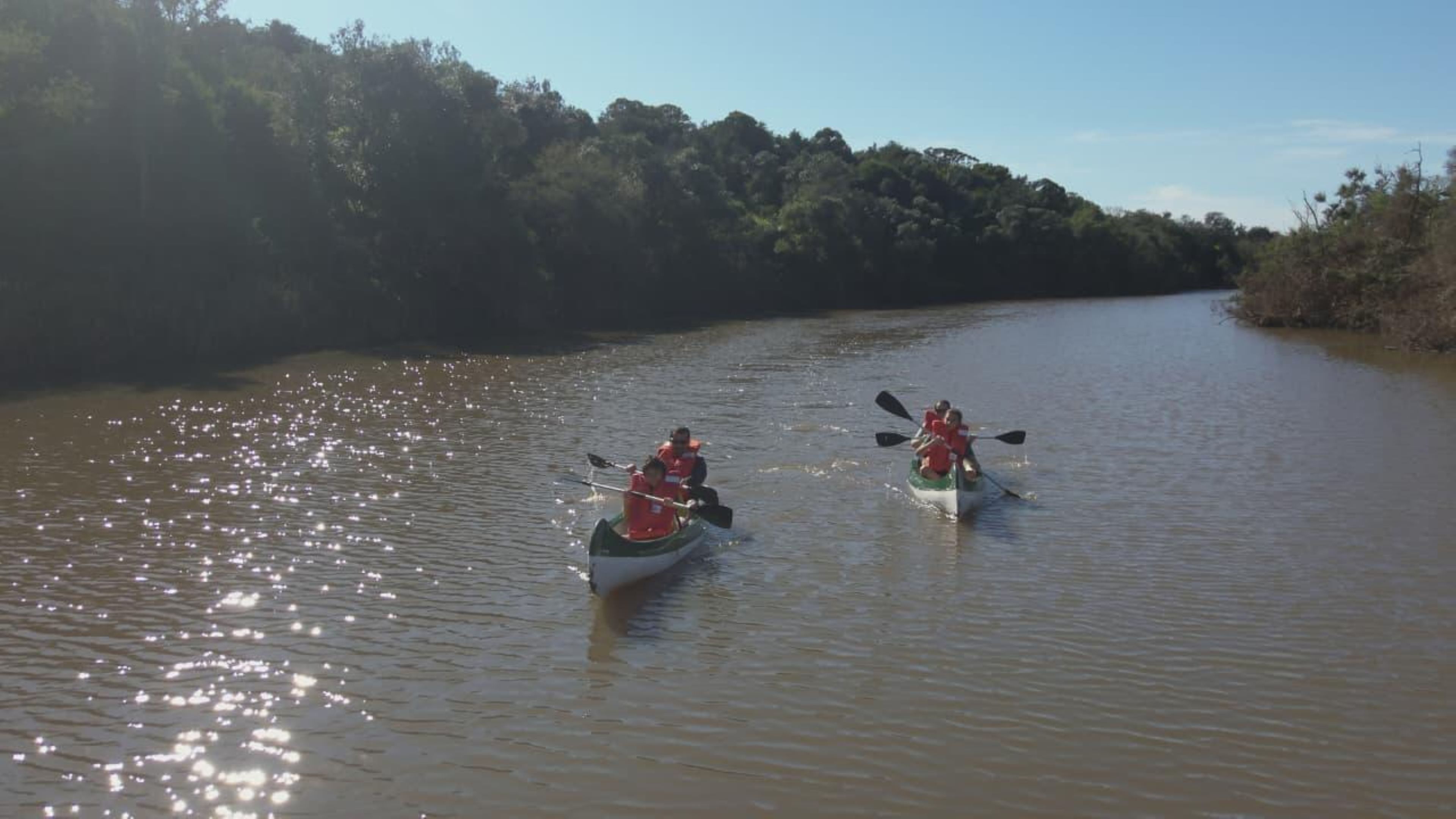 Two canoes on a calm river with dense foliage on the banks.