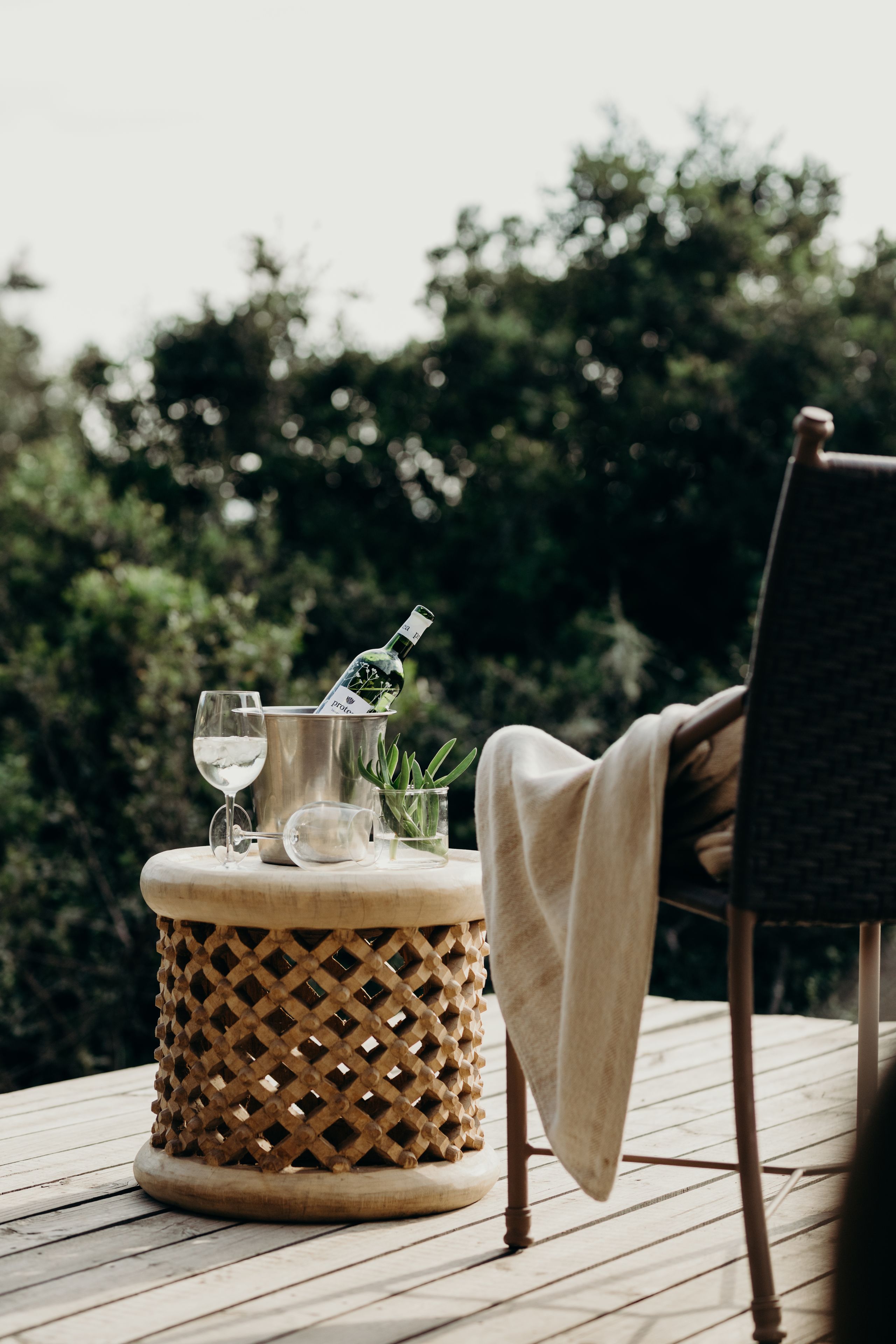 A wicker table with a bottle of wine, glasses, and a plant.