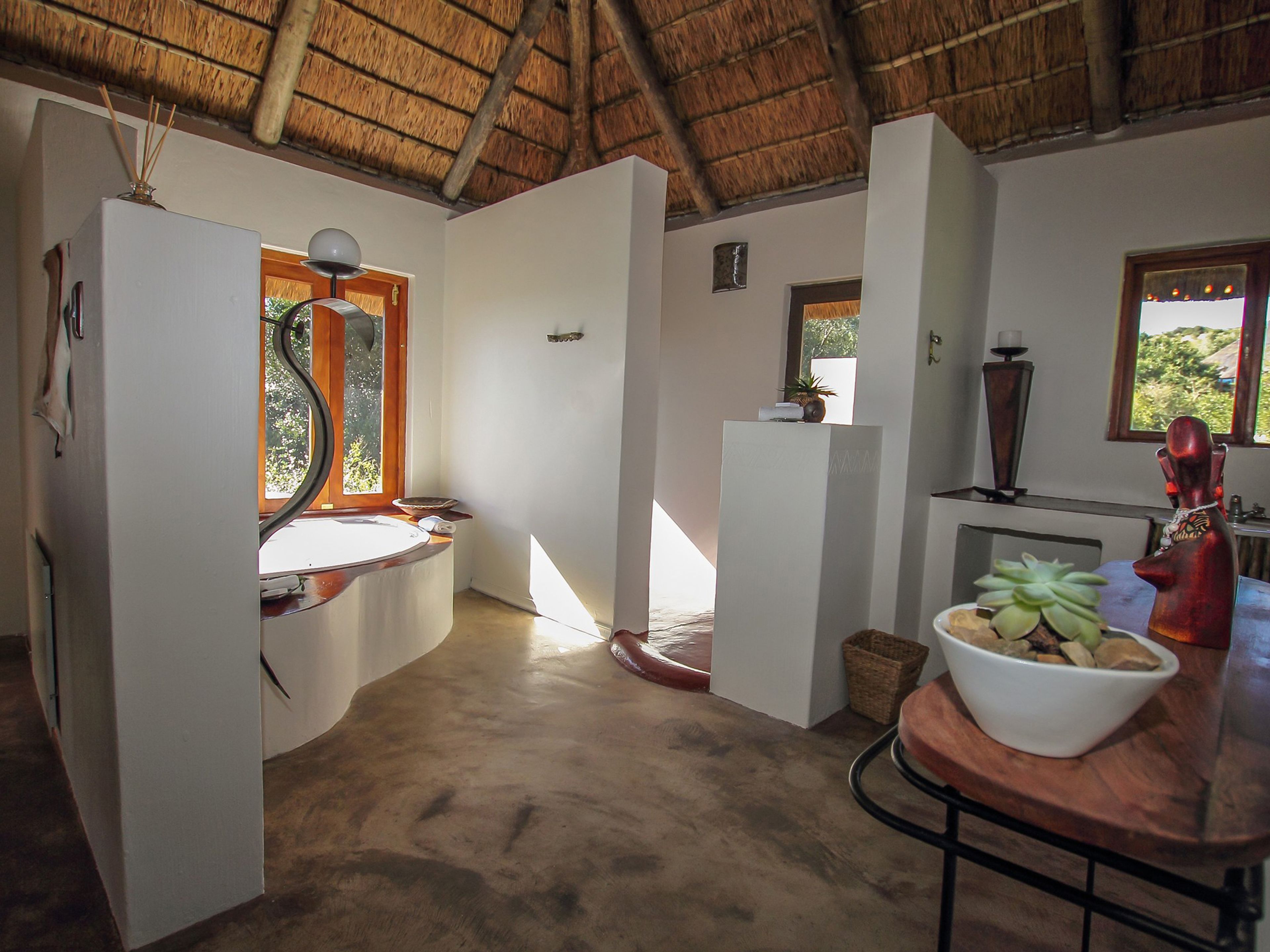 Una habitación con techo de paja, un lavabo, una mesa de madera con un cuenco de fruta y una ventana con vistas a la vegetación.