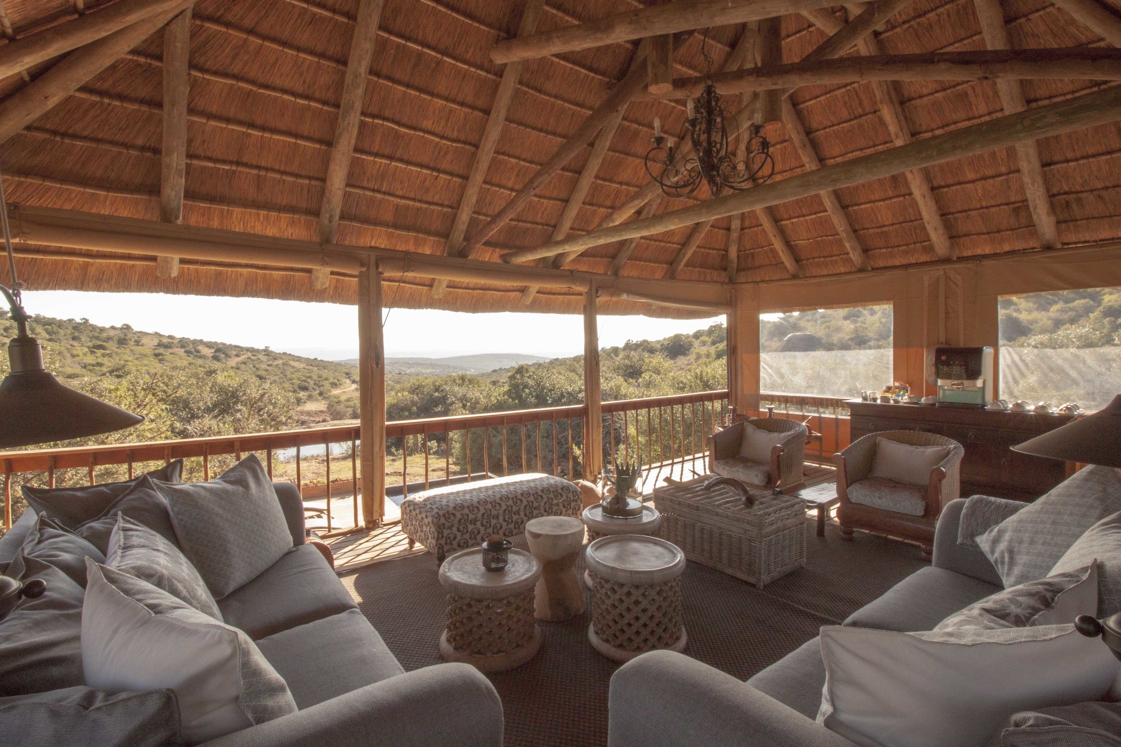 Un área de estar amplia al aire libre con techo de paja, mobiliario de mimbre y vistas a un paisaje montañoso.
