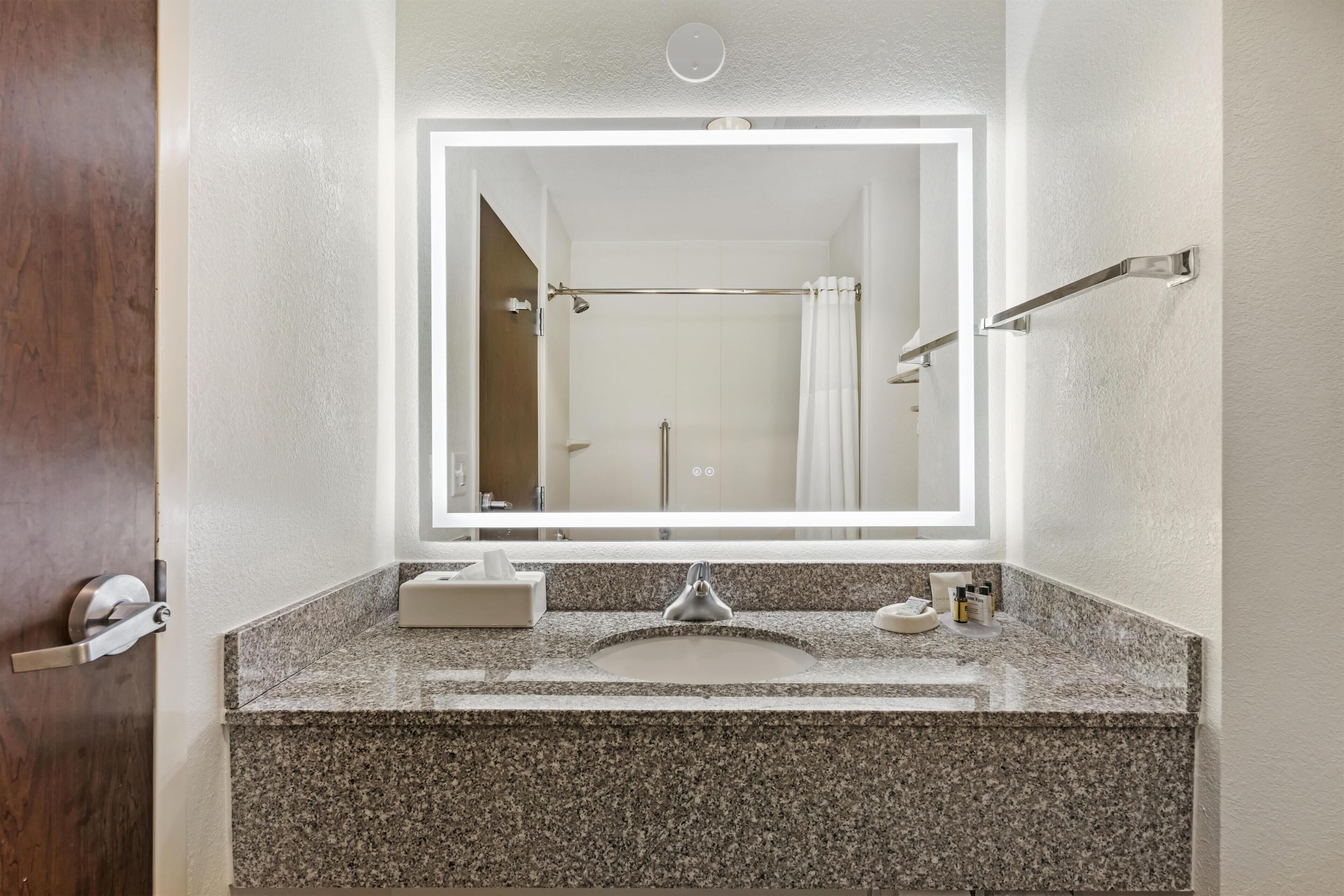 A bathroom with a granite countertop, a sink, a mirror, and a shower curtain.