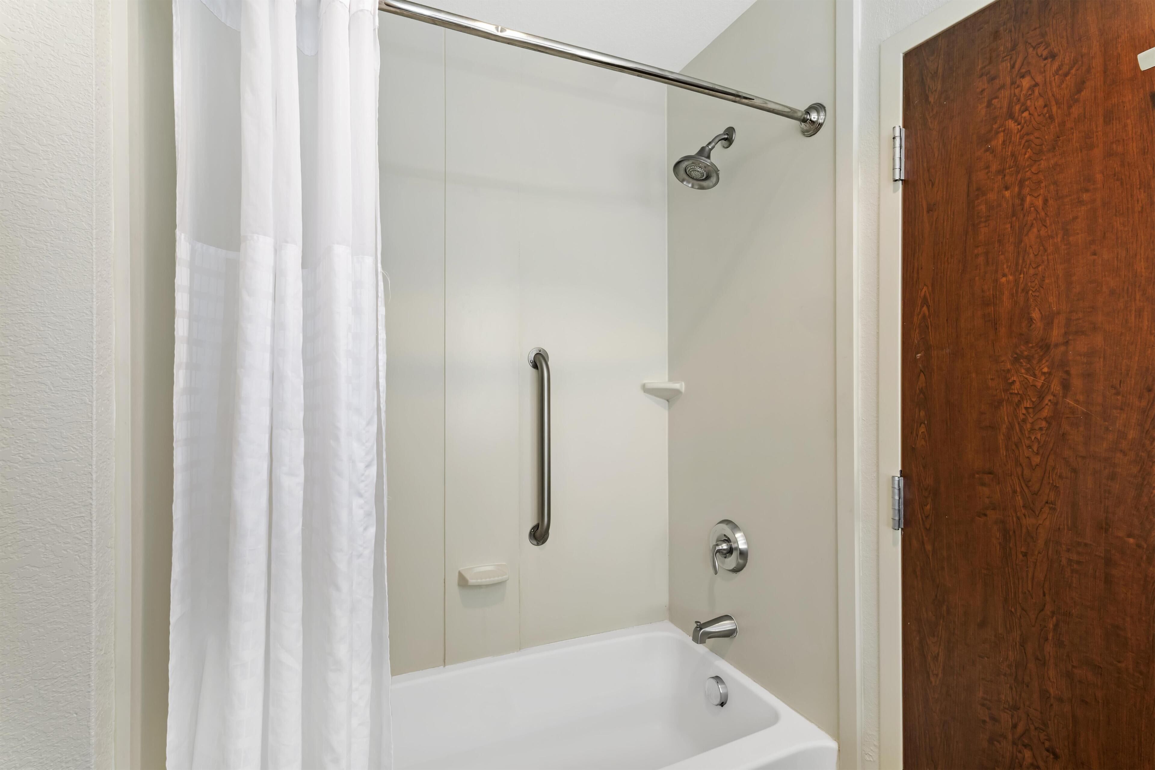 A shower with a glass door, a handrail, and a showerhead.