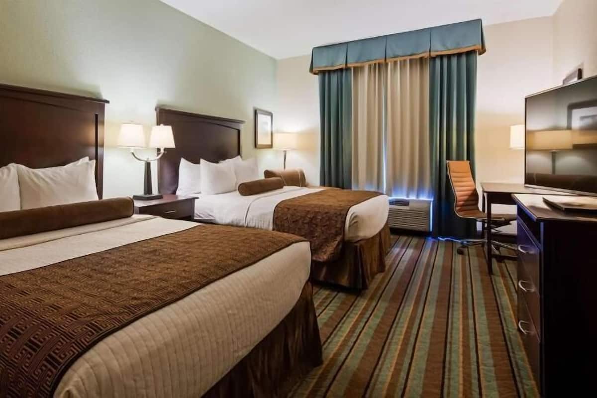 Une chambre d’hôtel avec deux lits, un bureau, une télévision et une fenêtre avec des rideaux.
