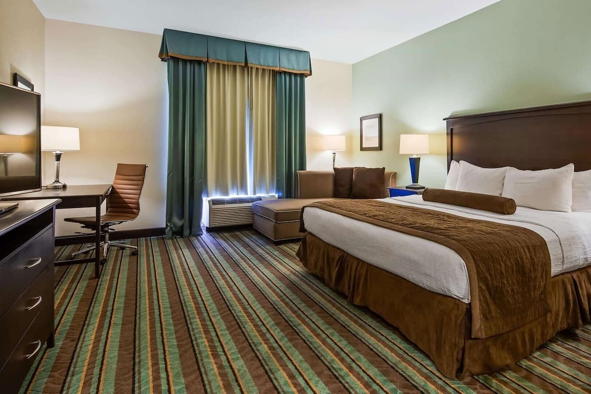 Une chambre d’hôtel avec un lit, un bureau, une chaise et une grande fenêtre avec des rideaux.