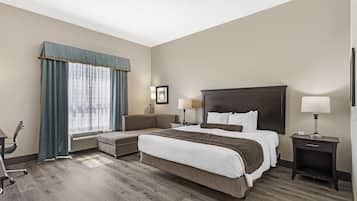 A hotel room with a large bed, a desk, a chair, a sofa, and a window with curtains.