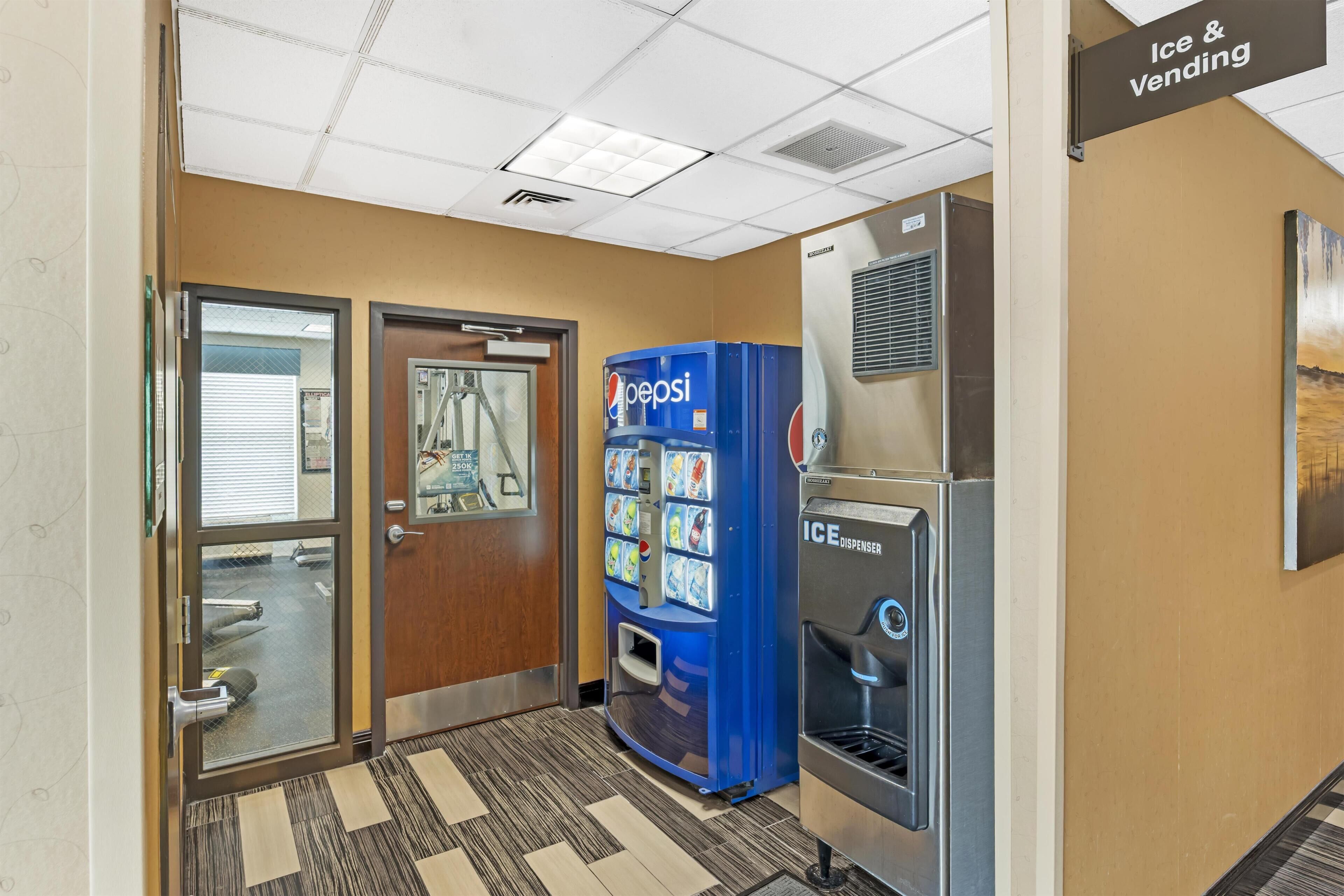A hallway with a Pepsi vending machine, an ice dispenser, and a door leading to a room.