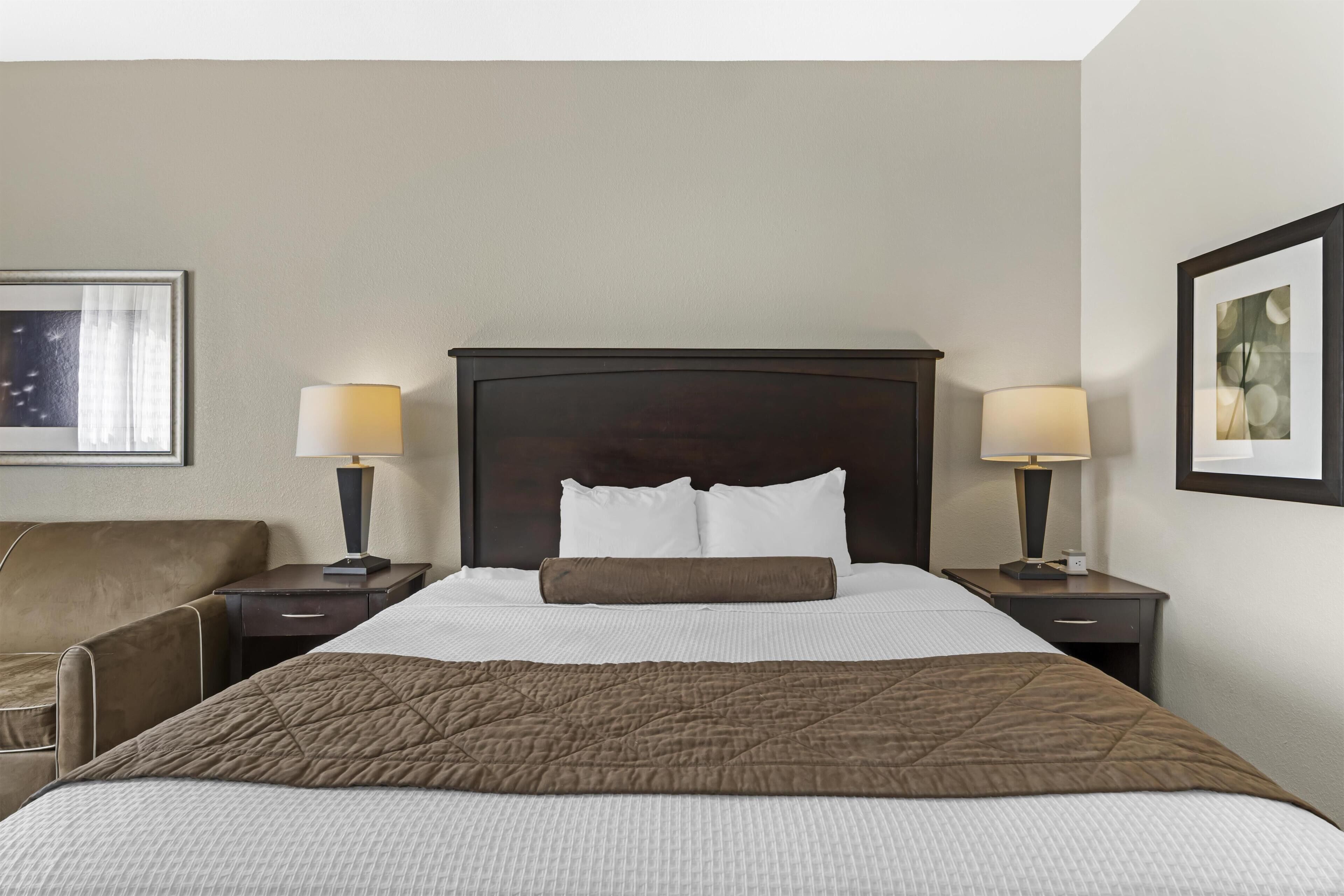 A hotel room with a large bed, two bedside tables, a chair, and artwork on the walls.