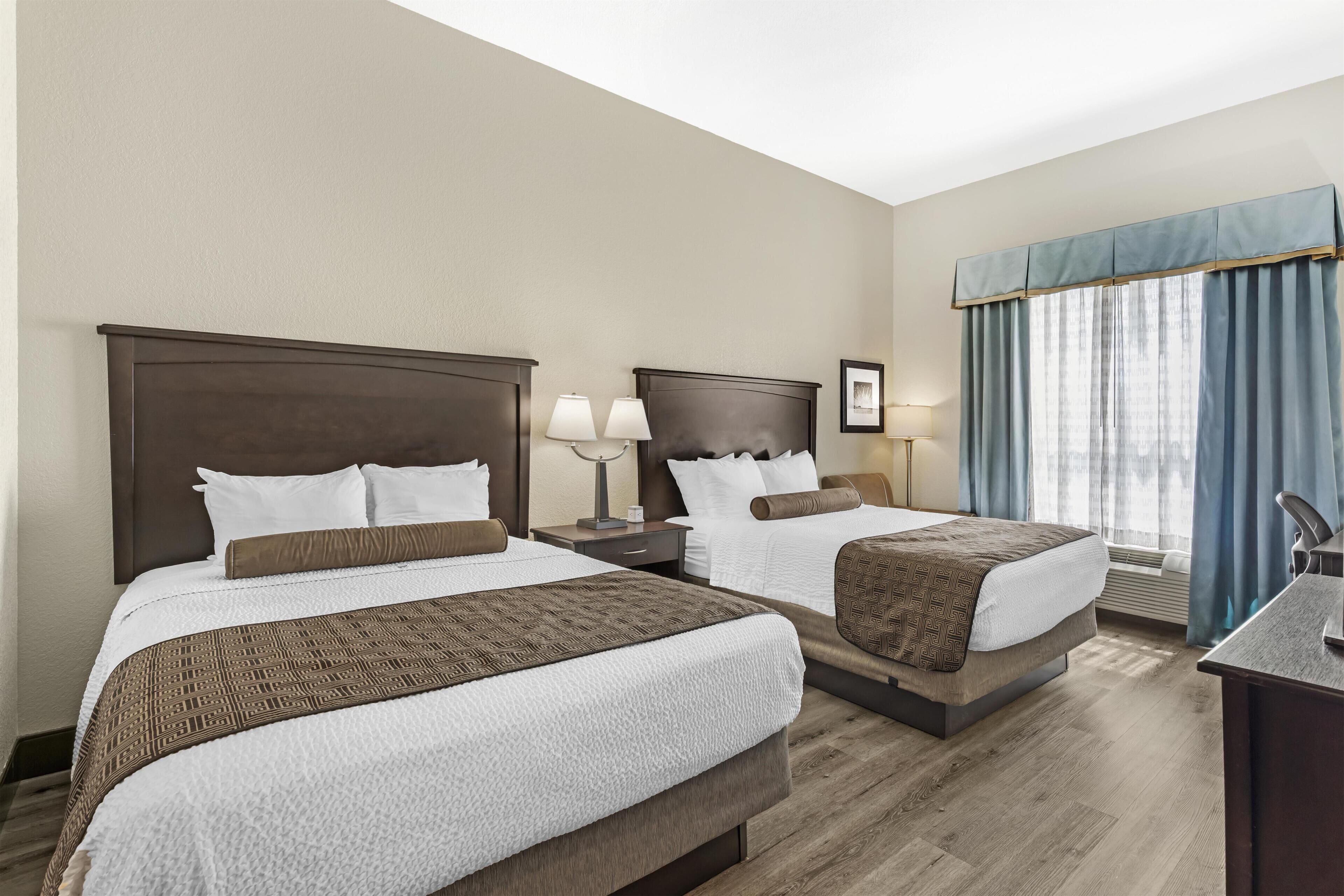 A hotel room with two beds, a desk, and a window with curtains.